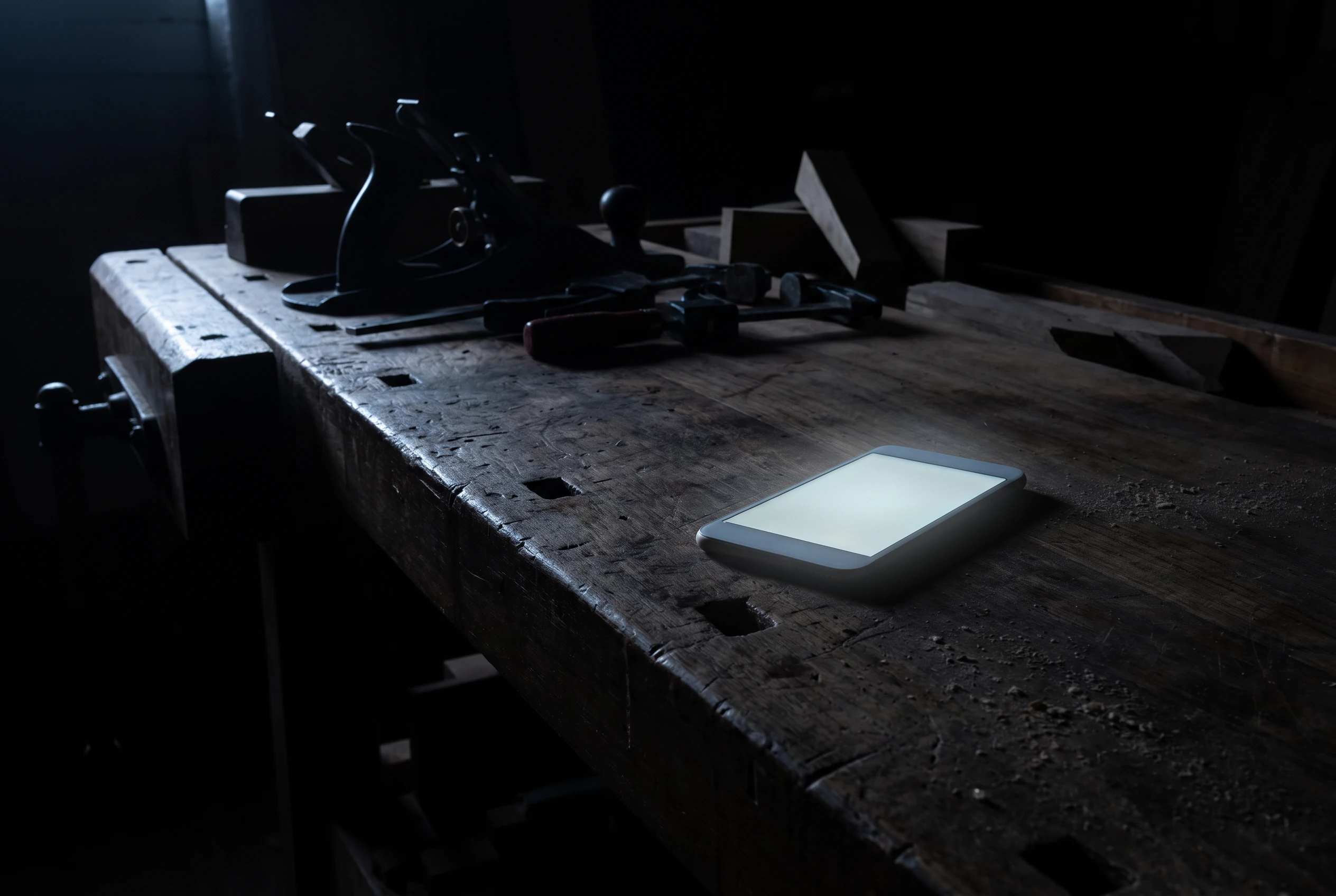 Werkbank einer Tischlerei bei Nacht, niemand da; auf der Bank leuchtet ein Telefon mit einer Anfrage