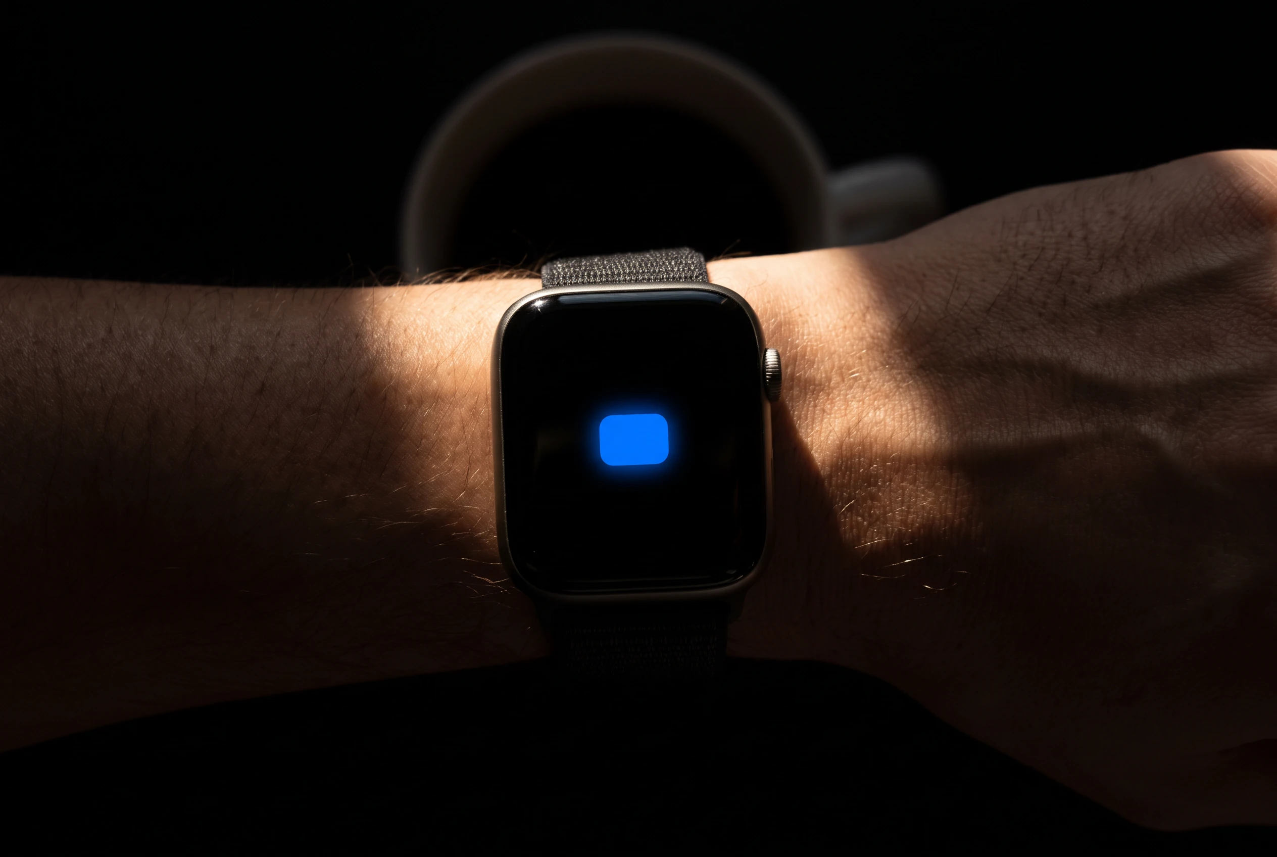 Handgelenk mit Uhr im ersten Morgenlicht, auf dem Zifferblatt leuchtet ein blauer Termin
